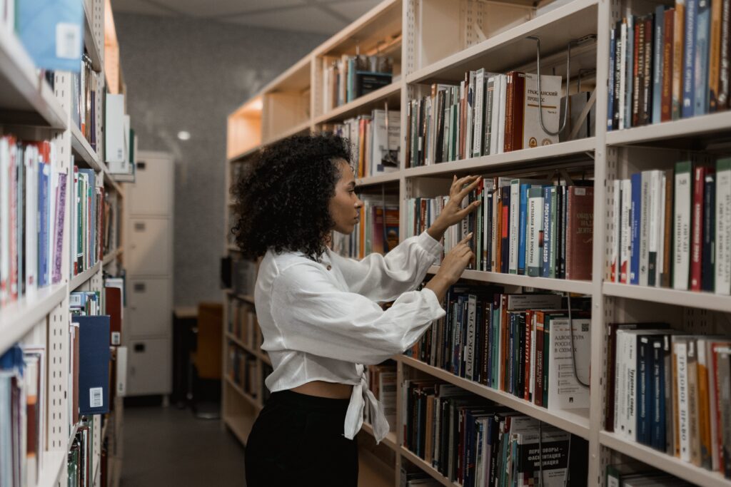 Kobieta w bibliotece szukająca książki na regle